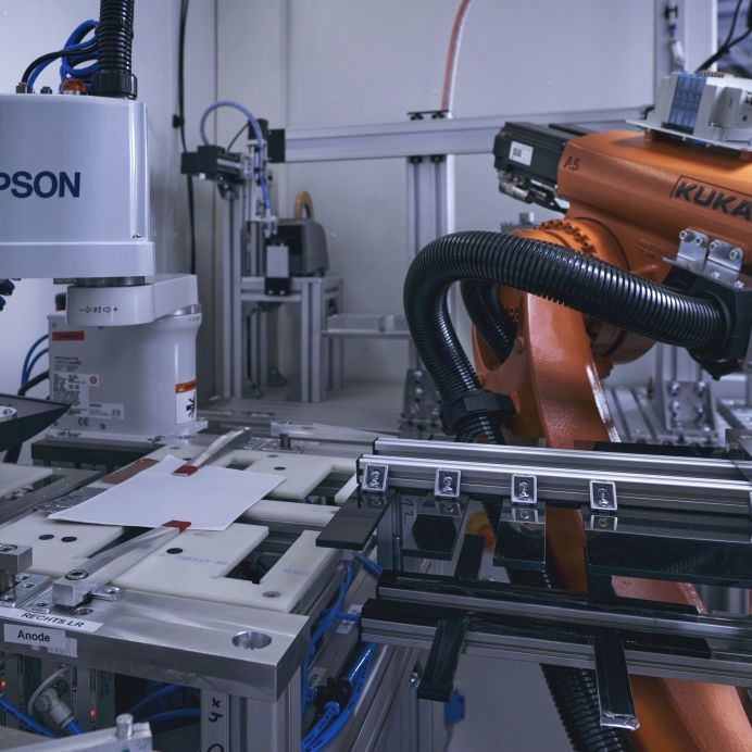 Interior view of the SmartBatteryMaker with the central robot and three production modules for stacking (left), contacting (center), and packaging (right).