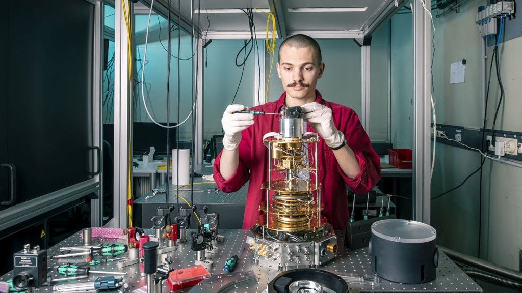 Ein KIT-Mitarbeiter integriert einen optischen Quantenspeicher in einen Kryostaten und koppelt ihn optisch per Glasfaser an ein supraleitendes Qubit.